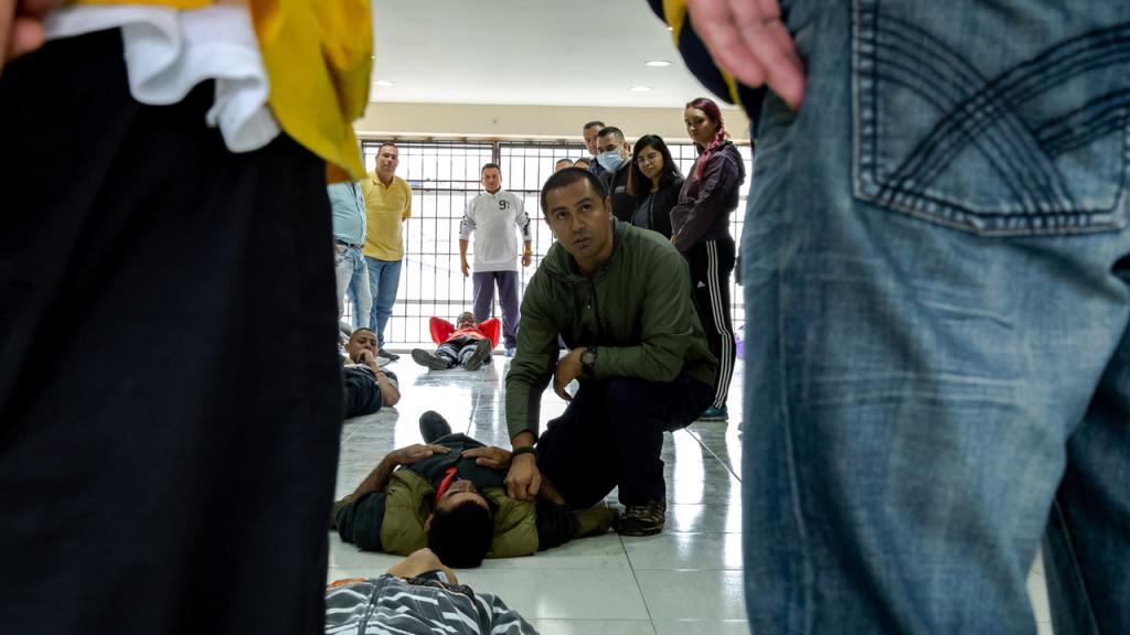 A man on his knees simulates providing medical care for someone. 