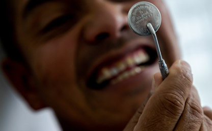 A man looks at his teeth in a dental mirror